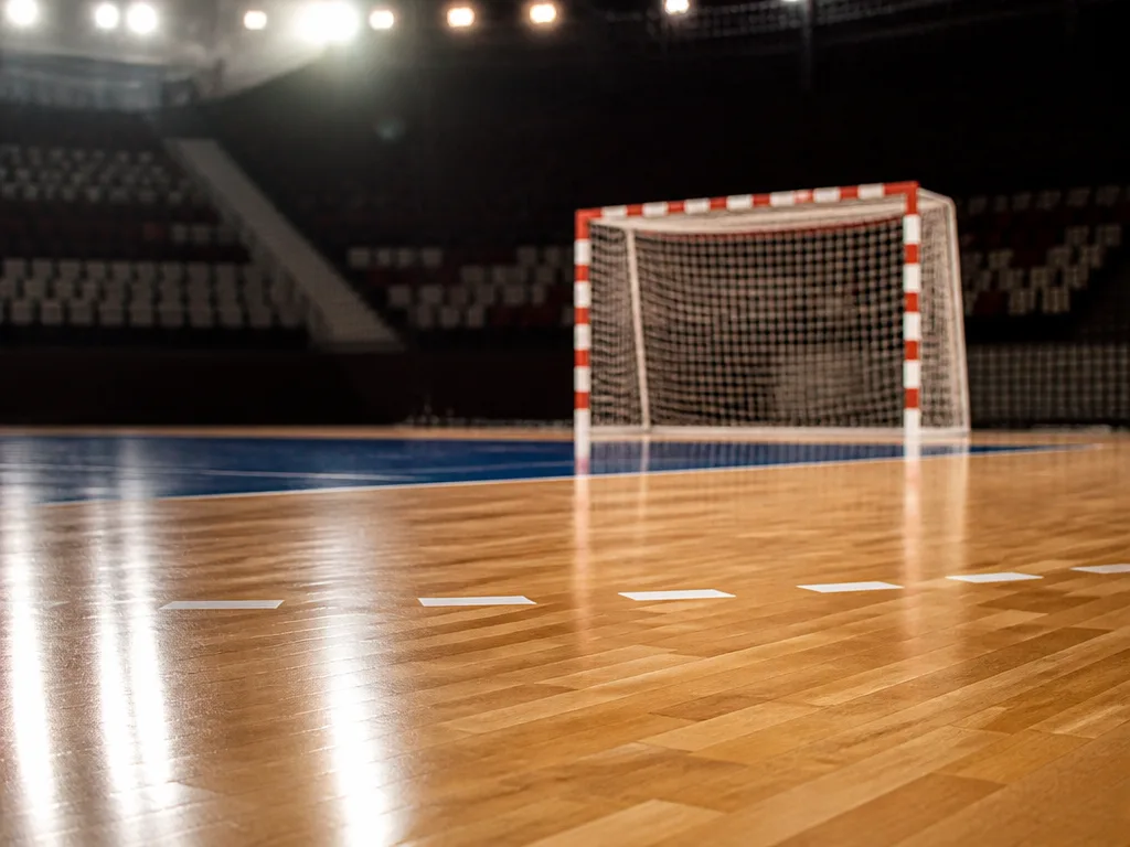 Tom handbollsplan i en arena med dramatisk belysning över mål och plan